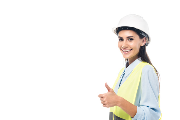 Usměvavý inženýr v tvrdé a bezpečnostní vestě ukazující na palec izolovaný na bílém - Fotografie, Obrázek