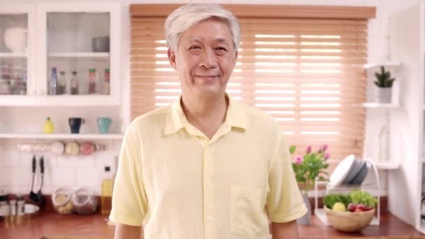 Ázsiai idős ember érzés boldog mosolygó és látszó-hoz fényképezőgép pihenés közben a konyhában otthon. Életmód Senior férfi otthon koncepció.  - Felvétel, videó