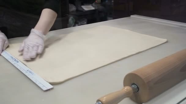 Η σκηνή: μάγειρας ευθυγραμμίζει το φύλλο ζύμης με ένα χάρακα, διαμόρφωση της ζύμης. Παραγωγή ρολά κανέλας. Προϊόντα αρτοποιίας. Κολλώδης ψωμάκια νόστιμα ψωμάκια κανέλλας  - Πλάνα, βίντεο
