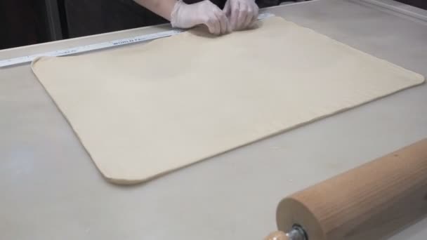 Η σκηνή: Cookaligns τη ζύμη φύλλο με ένα χάρακα, διαμόρφωση της ζύμης. Παραγωγή ρολά κανέλας. Προϊόντα αρτοποιίας. Κολλώδης ψωμάκια νόστιμα ψωμάκια κανέλλας  - Πλάνα, βίντεο