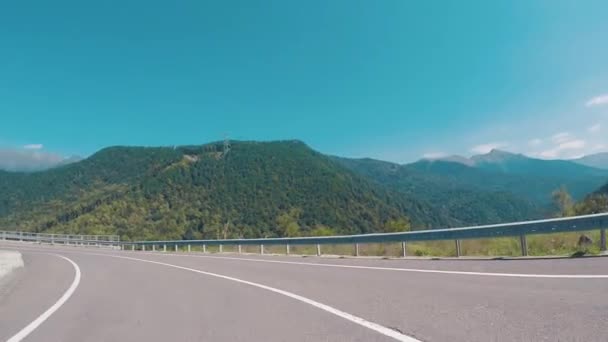Pintoresca vista sobre una carretera y montañas cubiertas de árboles desde el coche en movimiento contra el cielo azul. Escena. Montañas paisaje
. - Metraje, vídeo