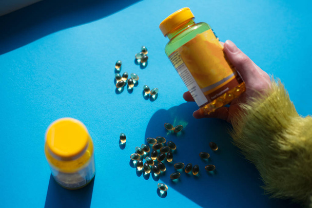 Entregar cápsulas de vitaminas amarelas sobre fundo azul
. - Foto, Imagem