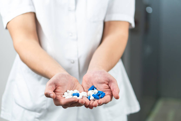 Bright close up of male doctor in uniform with stethoscope and holding blue and white pills in hands - Photo, Image
