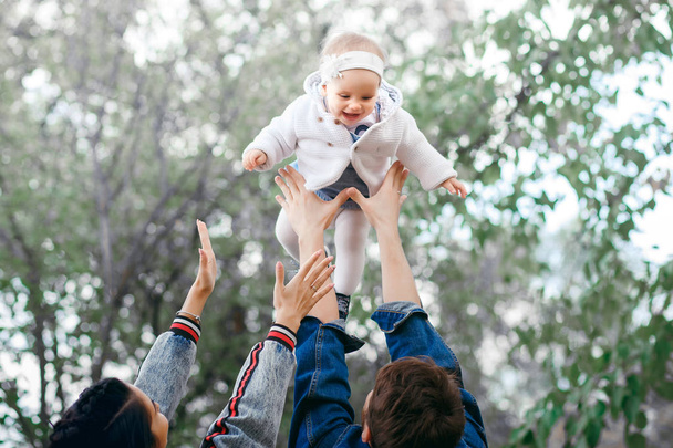 Família feliz ao ar livre atividade, pai levanta o bebê, rindo e brincando, pai mostra à mãe como jogar o bebê com segurança
 - Foto, Imagem