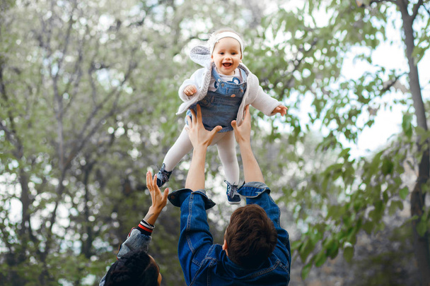 Família feliz ao ar livre atividade, pai levanta o bebê, rindo e brincando, pai mostra à mãe como jogar o bebê com segurança
 - Foto, Imagem
