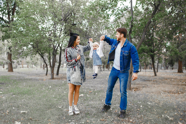 Семья гуляет в парке, мать держит маленькую дочь над головой, отец заботится о семье
 - Фото, изображение