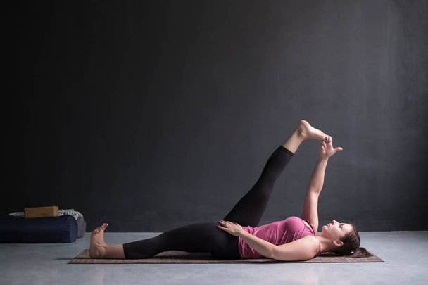 Женщина делает Yoga asana Supta padangusthasana или наклоняя руку к большой позе пальца ноги
 - Фото, изображение