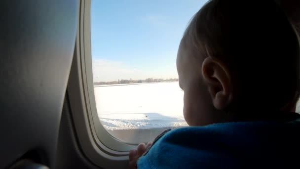 Ξανθιά μικρό αγόρι κάθεται κοντά στο παράθυρο του αεροπλάνου και φαίνεται. - Πλάνα, βίντεο