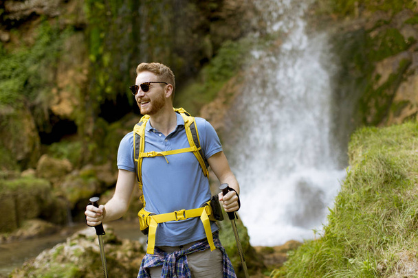 Hermoso joven excursionista se detuvo junto a una cascada de montaña para descansar
 - Foto, Imagen
