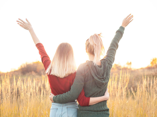 Two young women standing on the field and rise up hands. Best friends - Foto, imagen