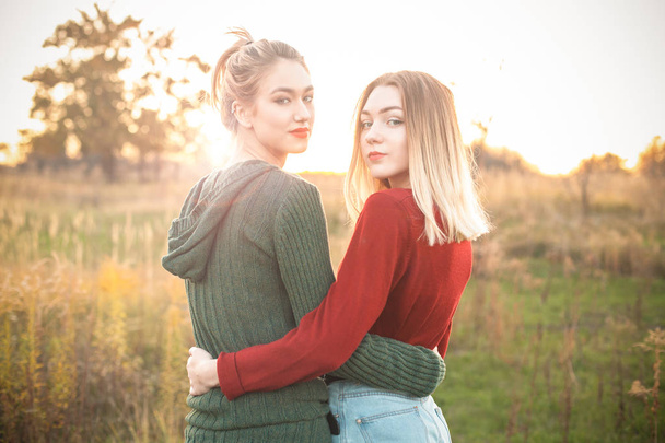 Two best friends walking on the field at sunset and hugging - Zdjęcie, obraz