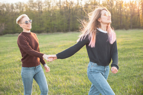 Two beautiful young women walking on the grass field - Foto, afbeelding