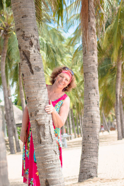 Portrait of a smiling happy senior woman standing near the palm tree - Foto, afbeelding