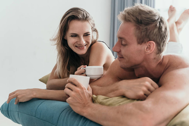 couple lying on bed and having a cup of coffee - 写真・画像