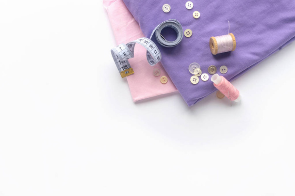 Sewing accessories and fabric on a white background. Fabric, sewing threads, needle, buttons and sewing centimeter. top view, flatlay - Photo, Image