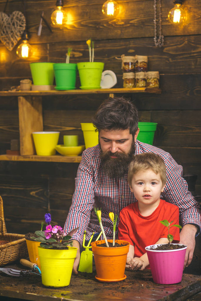 Family day. Greenhouse. bearded man and little boy child love nature. Flower care watering. Soil fertilizers. happy gardeners with spring flowers. Father and son. Fathers day. Joyful process - Фото, зображення