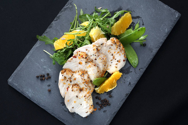 Poultry fillet on a salad with sugar peas and oranges on a black plate. - Photo, Image