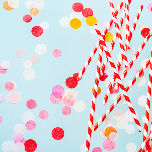 Red striped drinking straws for beverage and colored confetti on pastel blue background - Фото, изображение
