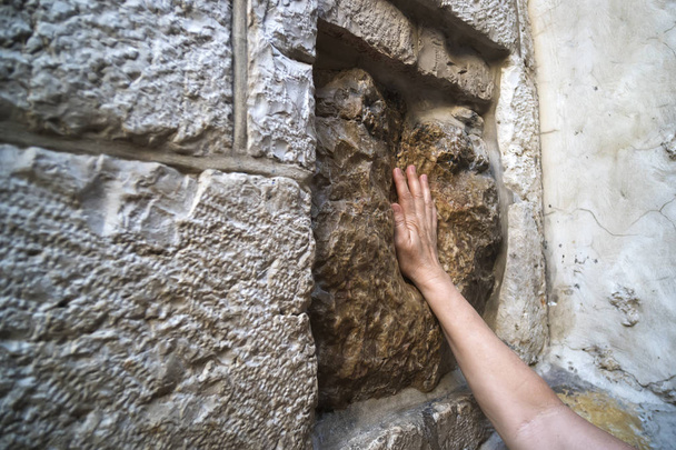 イエスの手の押印をするといわれる空洞で古い正方形石に触れる若い男の手のクローズ アップ。5 つの駅でイエスの手形。ヴィア ・ ドロローサ、エルサレム、イスラエル共和国。壁. - 写真・画像