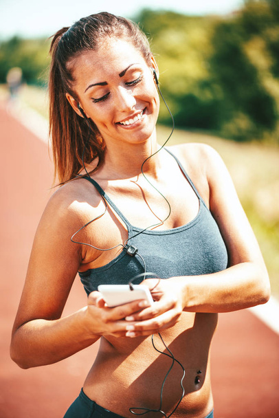 Mujer joven sonriente escuchando música en los auriculares y descansando después de trotar
 - Foto, Imagen