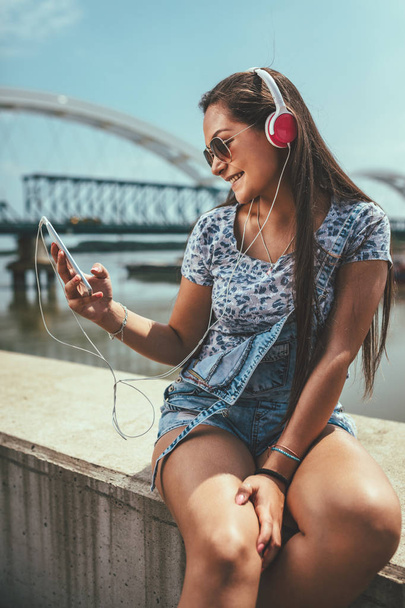 cheerful young woman listening music from smartphone on riverbank - Foto, Bild
