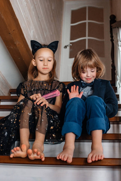 brother and sister sitting on stairs in festive clothes while playing with hand fan - Фото, зображення