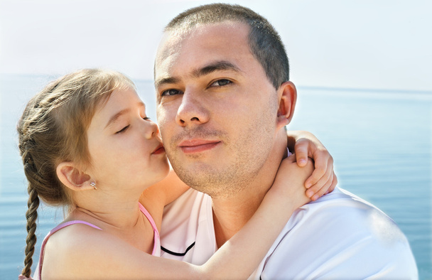 Маленька дівчинка цілує батька на пляжі
 - Фото, зображення