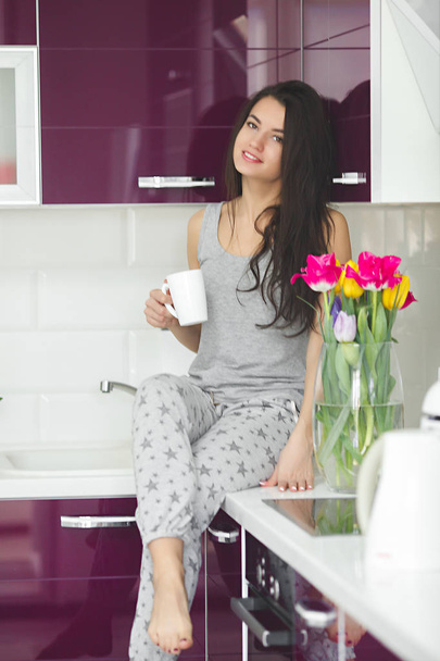 Young beautiful woman in the early morning having coffee on the kitchen. Fresh morning.  Bracing drink. Fees for work. Awake lady. - Zdjęcie, obraz