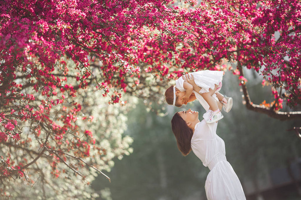 Młoda kochająca matka spacerująca ze swoim małym dzieckiem na wiosennym tle. Cute dziecko i jej mama na świeżym powietrzu.Rodzina w parku. - Zdjęcie, obraz