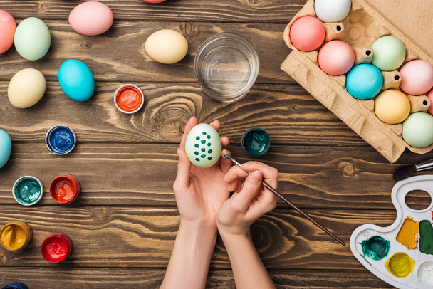 vágott kilátás nő díszítő húsvéti tojás, ecset, fából készült asztal színt a palettáról és festékek - Fotó, kép