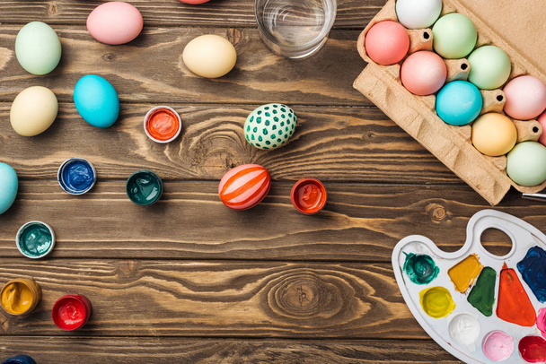 Ansicht von bemalten Ostereiern, Farbpalette und Acrylfarben auf Holzoberfläche - Foto, Bild