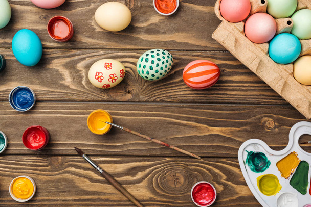vista superior de huevos de Pascua pintados, paleta de colores y pinturas acrílicas en la superficie de madera
 - Foto, imagen