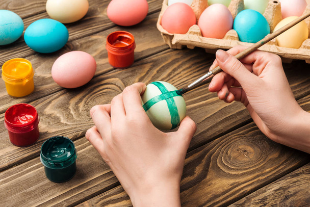 partial view of girl decorating easter eggs with paintbrush at wooden table - Фото, изображение