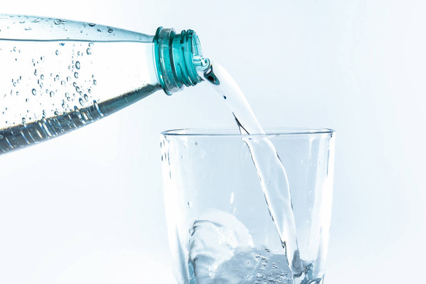 Wylewanie wody z butelki do kieliszka na białym tle - Zdjęcie, obraz