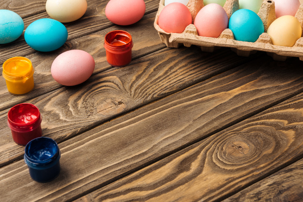 pastel easter eggs in cardboard box with acrylic paints on wooden table with copy space - Fotoğraf, Görsel