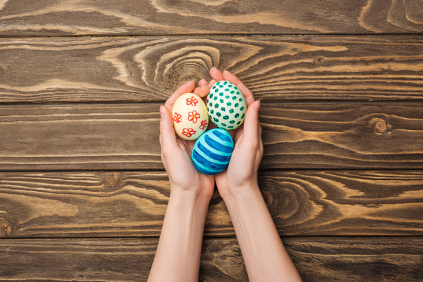 top view of woman holding easter eggs with pattern on wooden surface - Foto, immagini
