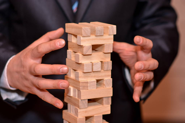 Alternatív kockázat fogalmát, terv és az üzleti stratégia. Üzletember kézzel kipróbálás-hoz tart egy torony fából készült blokk. - Fotó, kép
