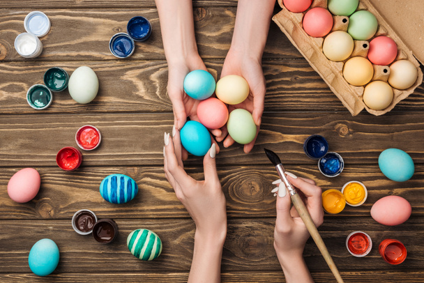 top view of women holding and painting easter eggs at wooden table - Foto, afbeelding