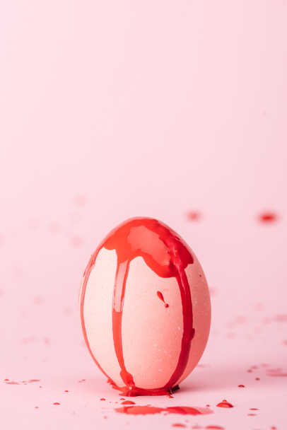 easter egg with red paint spills on pink with copy space - Fotó, kép