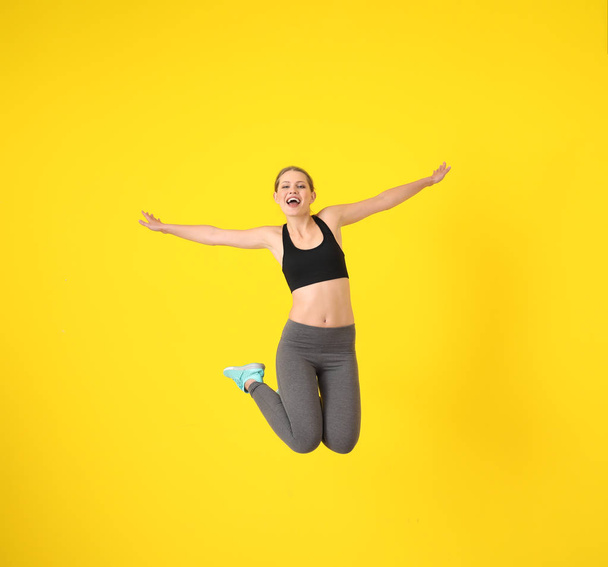 Young sporty woman jumping against color background - Foto, afbeelding
