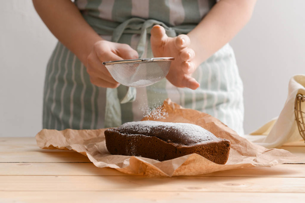 Woman sprinkling sugar powder onto tasty homemade cake on table - Valokuva, kuva