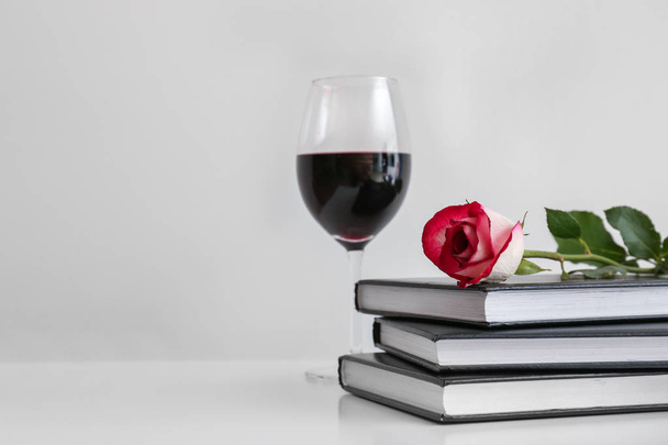 Bücher, Rosenblume und ein Glas Wein auf dem Tisch - Foto, Bild