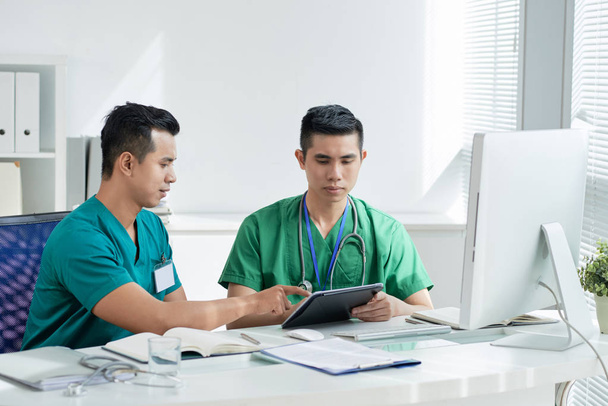 Jovens médicos vietnamitas discutindo informações em tablet digital
 - Foto, Imagem