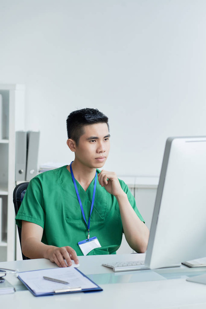 Zamyślony młode Azjatki pracownika medycznego czytanie e-maili na ekranie komputera - Zdjęcie, obraz