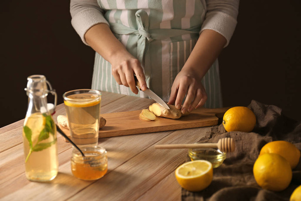 Woman cutting ginger for natural beverage on wooden table - Photo, image
