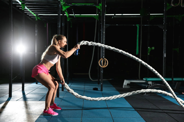 Jovem mulher esportiva fazendo exercício de corda de batalha no ginásio
 - Foto, Imagem
