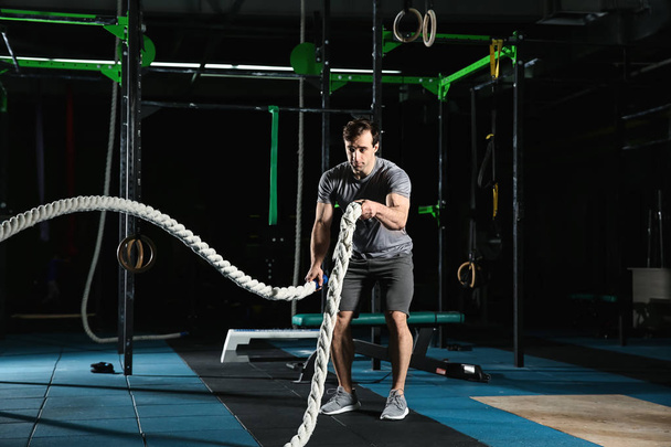 Young sporty man doing battle rope exercise in gym - Photo, Image