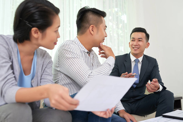 Smiling Vietnamese real estate broker consulting young couple at meeting - Photo, Image