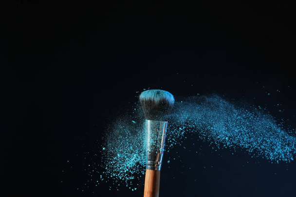 Makeup brush and burst of eyeshadows on dark background - Фото, изображение