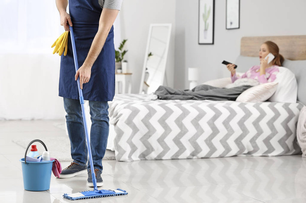 Househusband cleaning floor near lazy wife lying in bed - Photo, Image